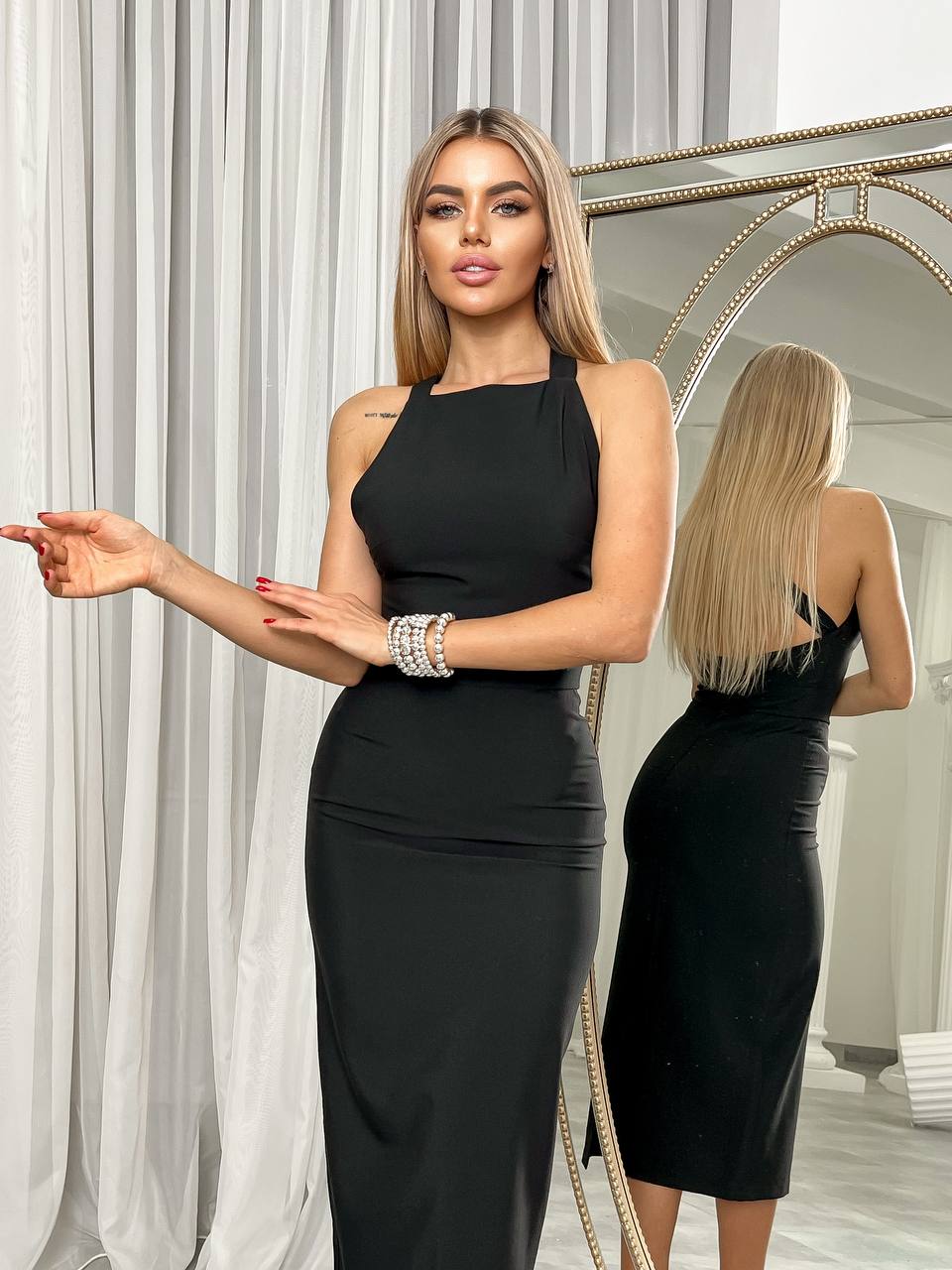 Woman wearing a black dress standing in front of a mirror.