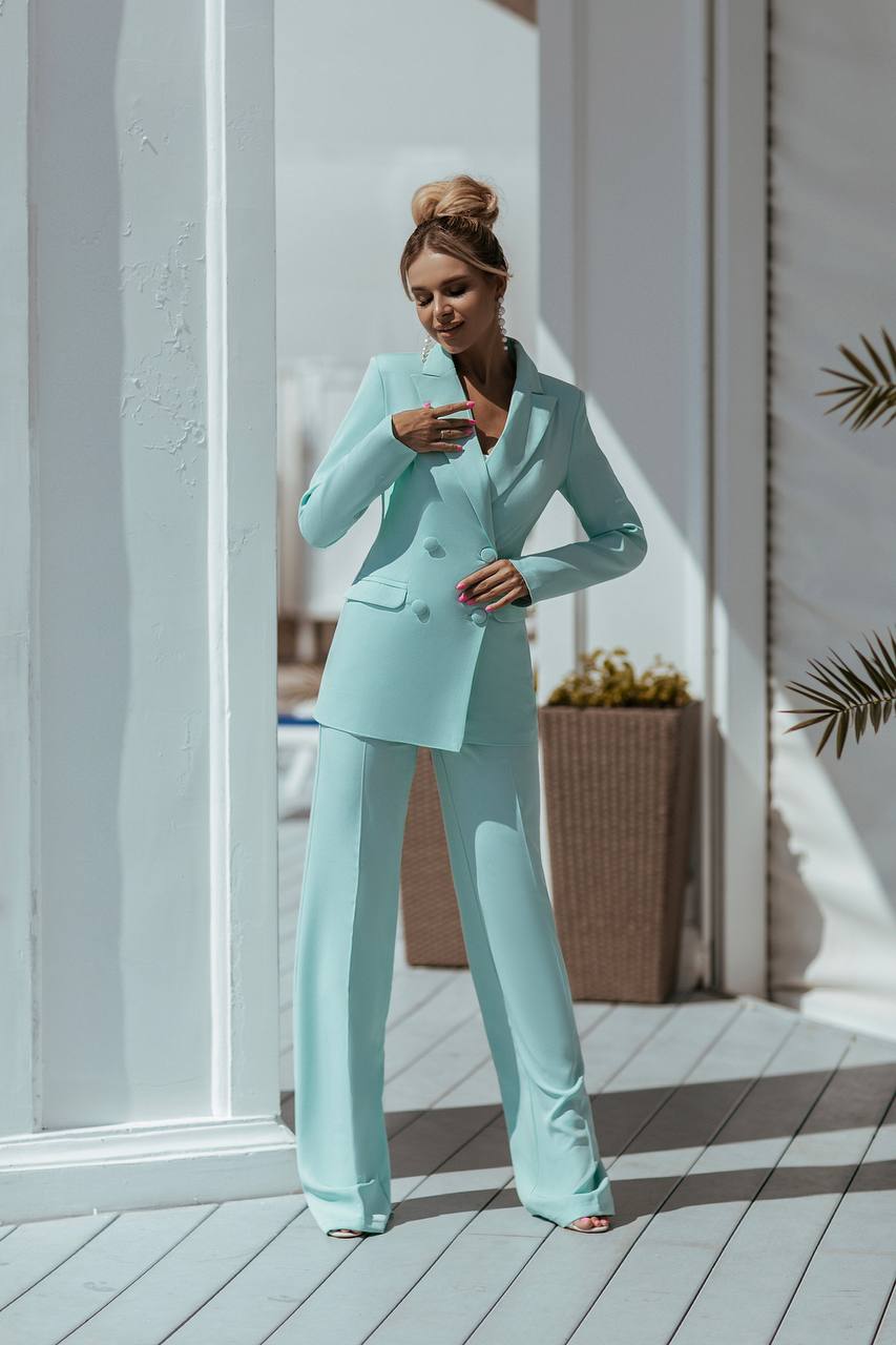 Woman in a light blue suit standing on a wooden deck with a neutral background