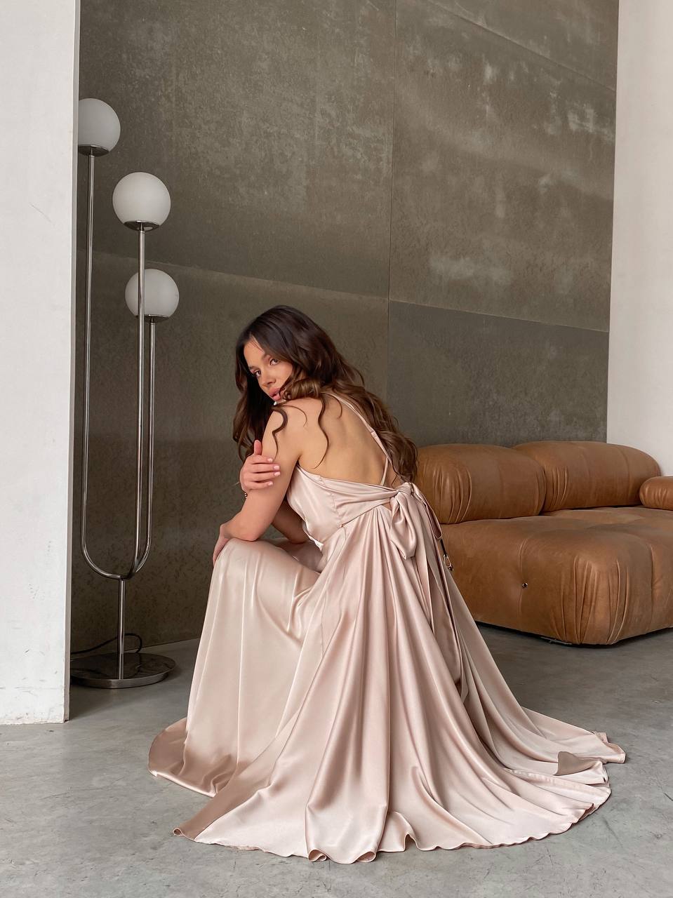 Woman in a flowing dress sitting on the floor in a modern interior setting.