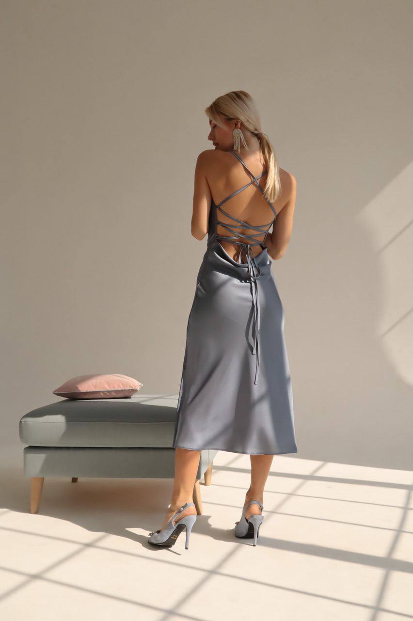 Woman in a gray slip dress standing in a sunlit room with a neutral color palette.