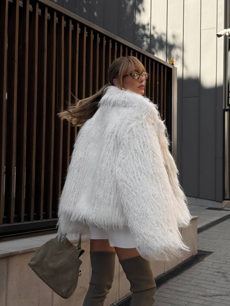 Woman wearing a white fluffy coat walking outdoors.