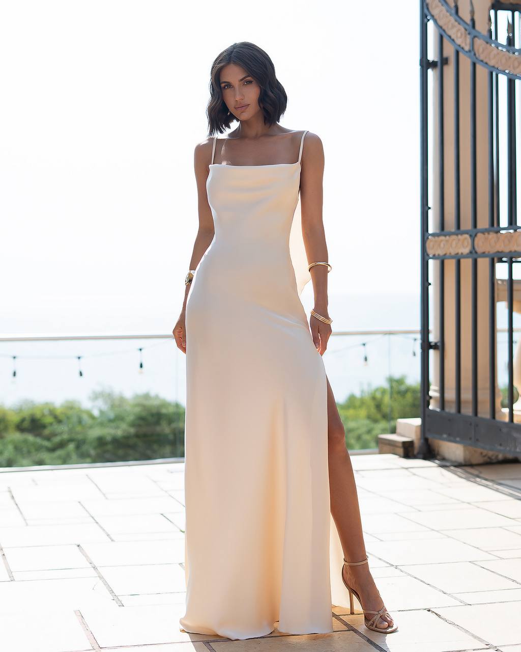 Woman in a white evening gown standing on a rooftop with a scenic background