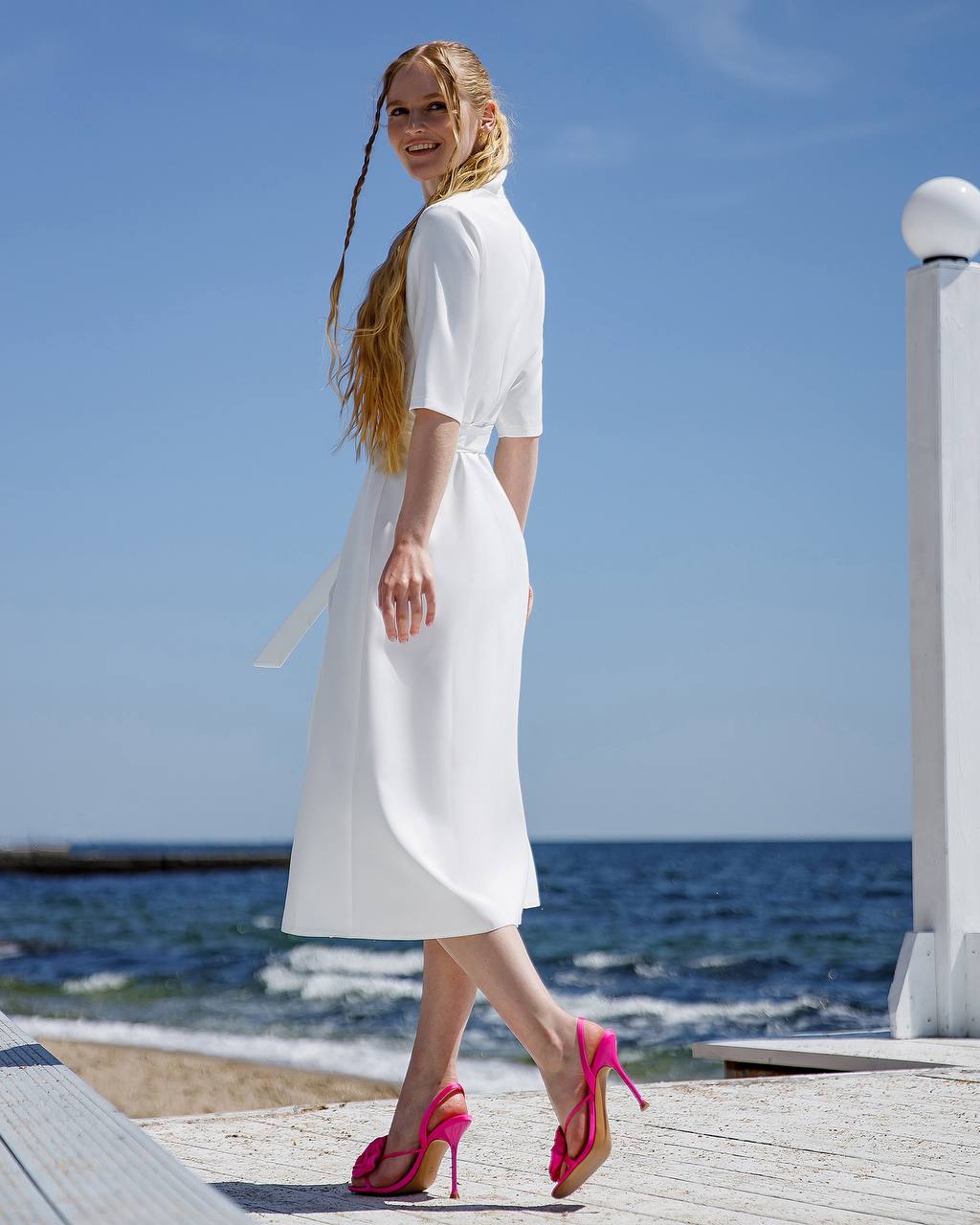 Woman in a white dress standing by the sea with a clear blue sky.