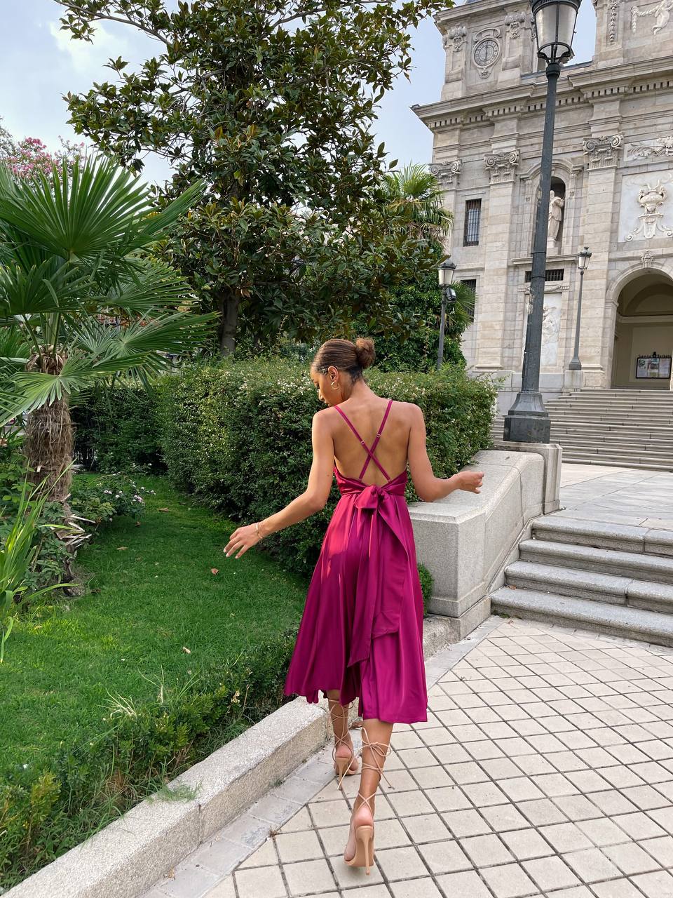 Woman in a pink dress walking in a garden with a building in the background