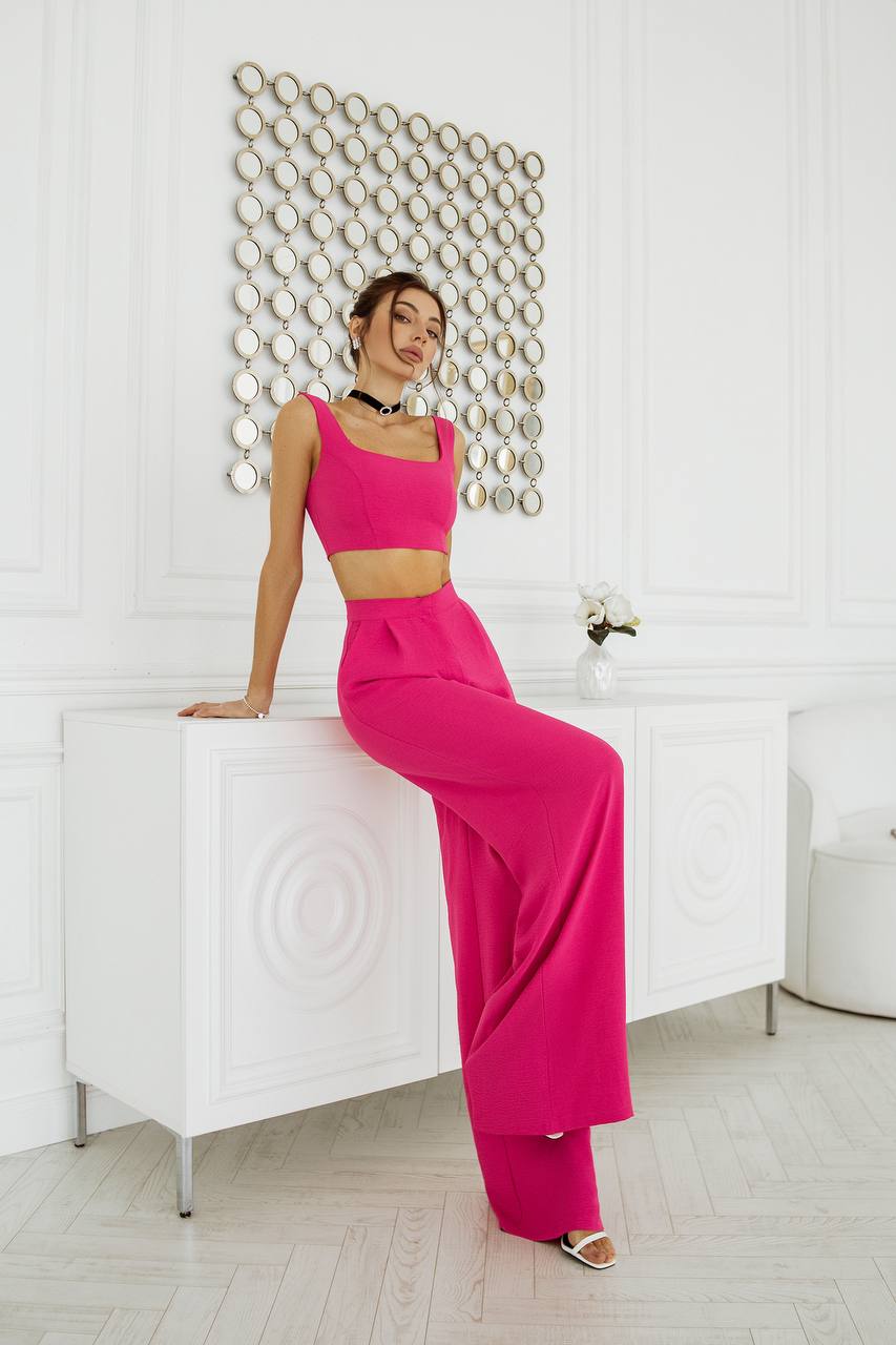 Woman in a bright pink outfit posing in a stylish interior setting.