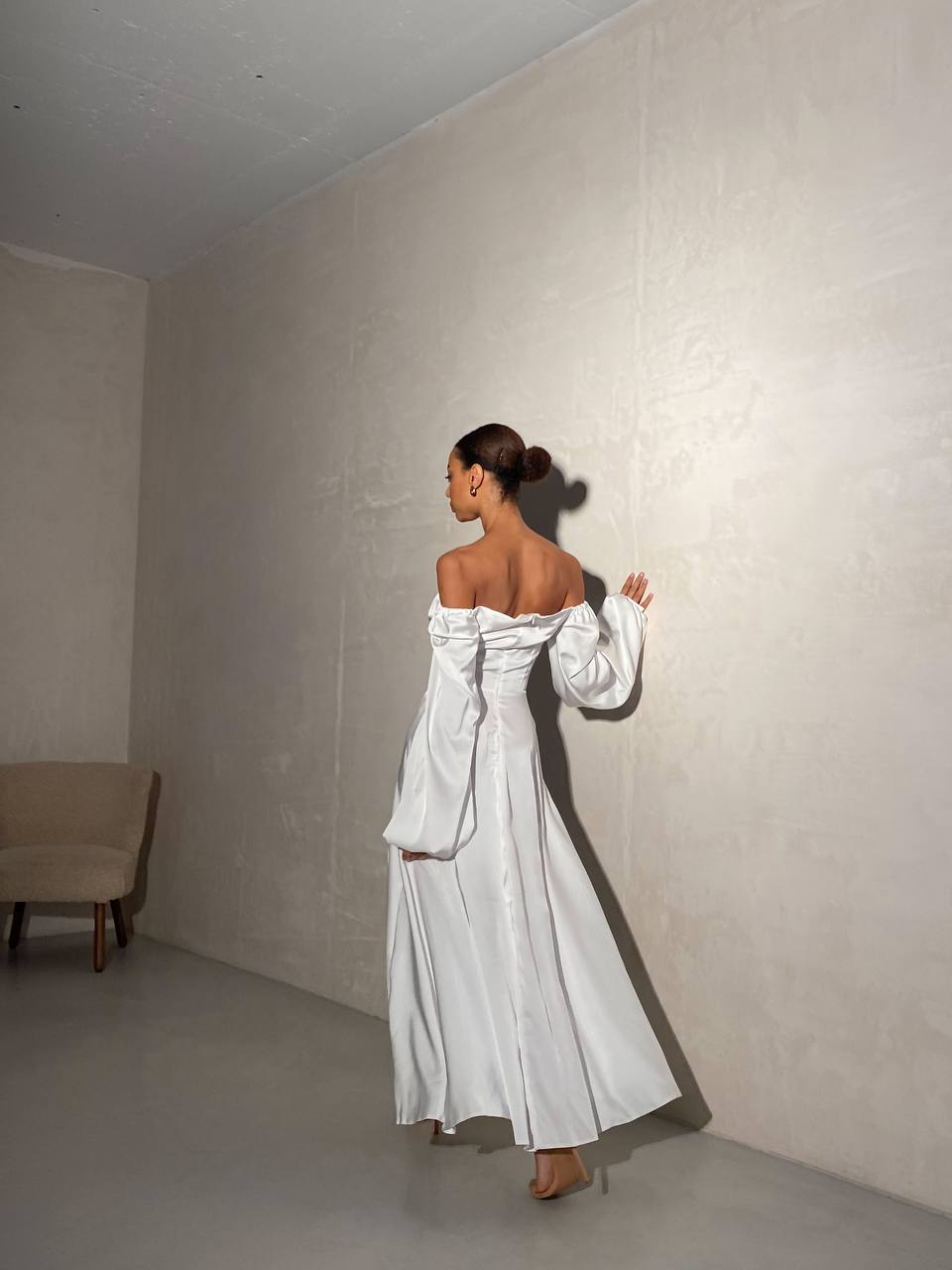 Woman in a white off-shoulder dress standing in a minimalistic room.
