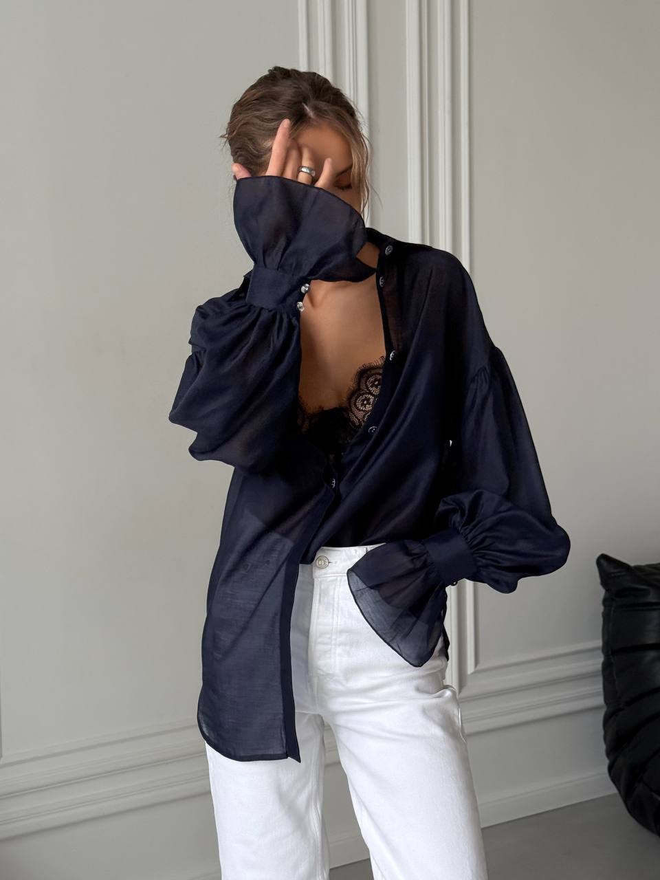 Person wearing a dark blue blouse with bow details and white pants in an indoor setting.