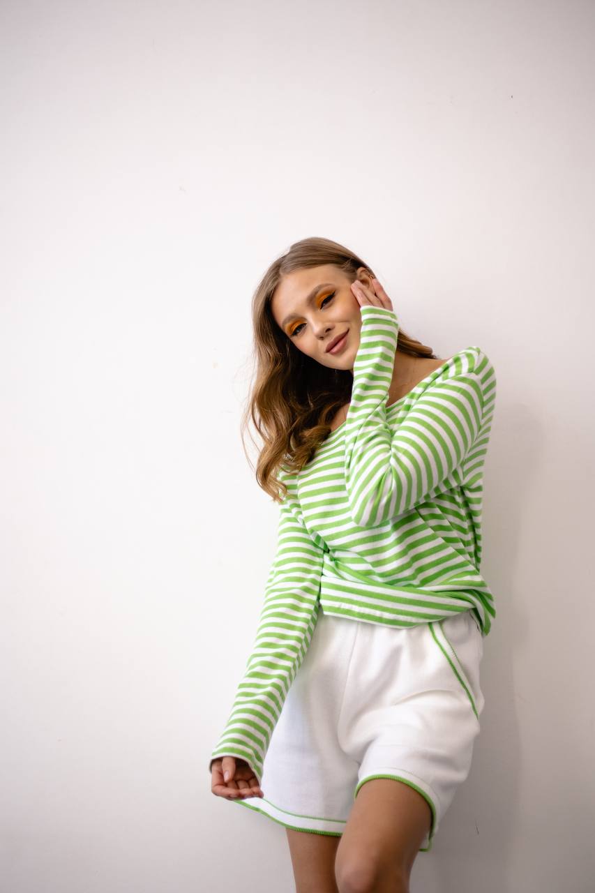 Woman wearing a green and white striped shirt and white shorts against a plain background