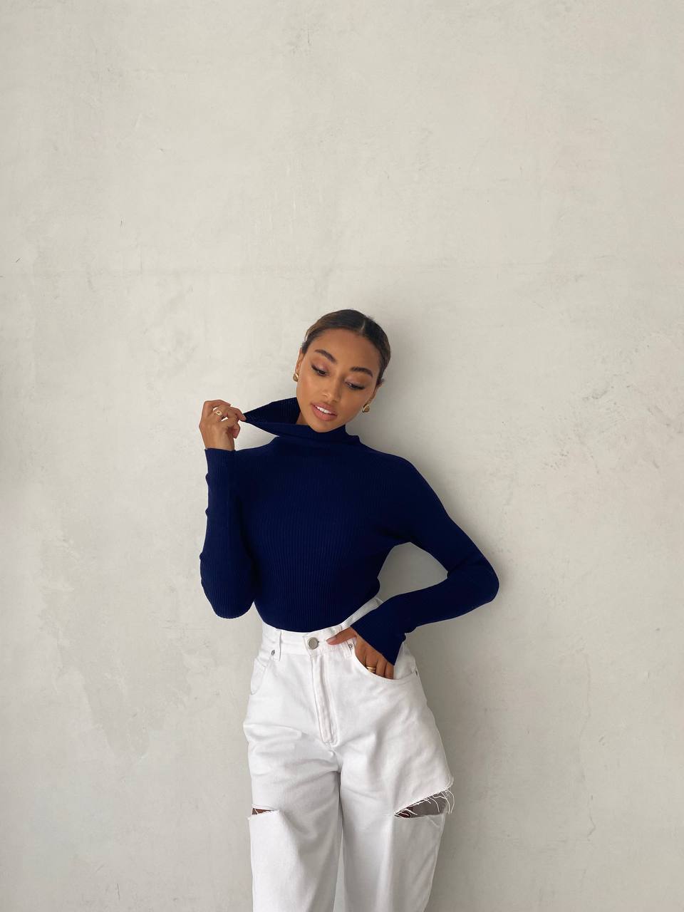 Person wearing a navy turtleneck and white pants against a plain background