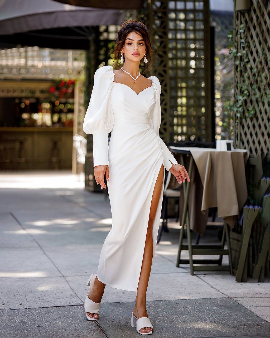 Woman in a white dress with a high slit walking outdoors.