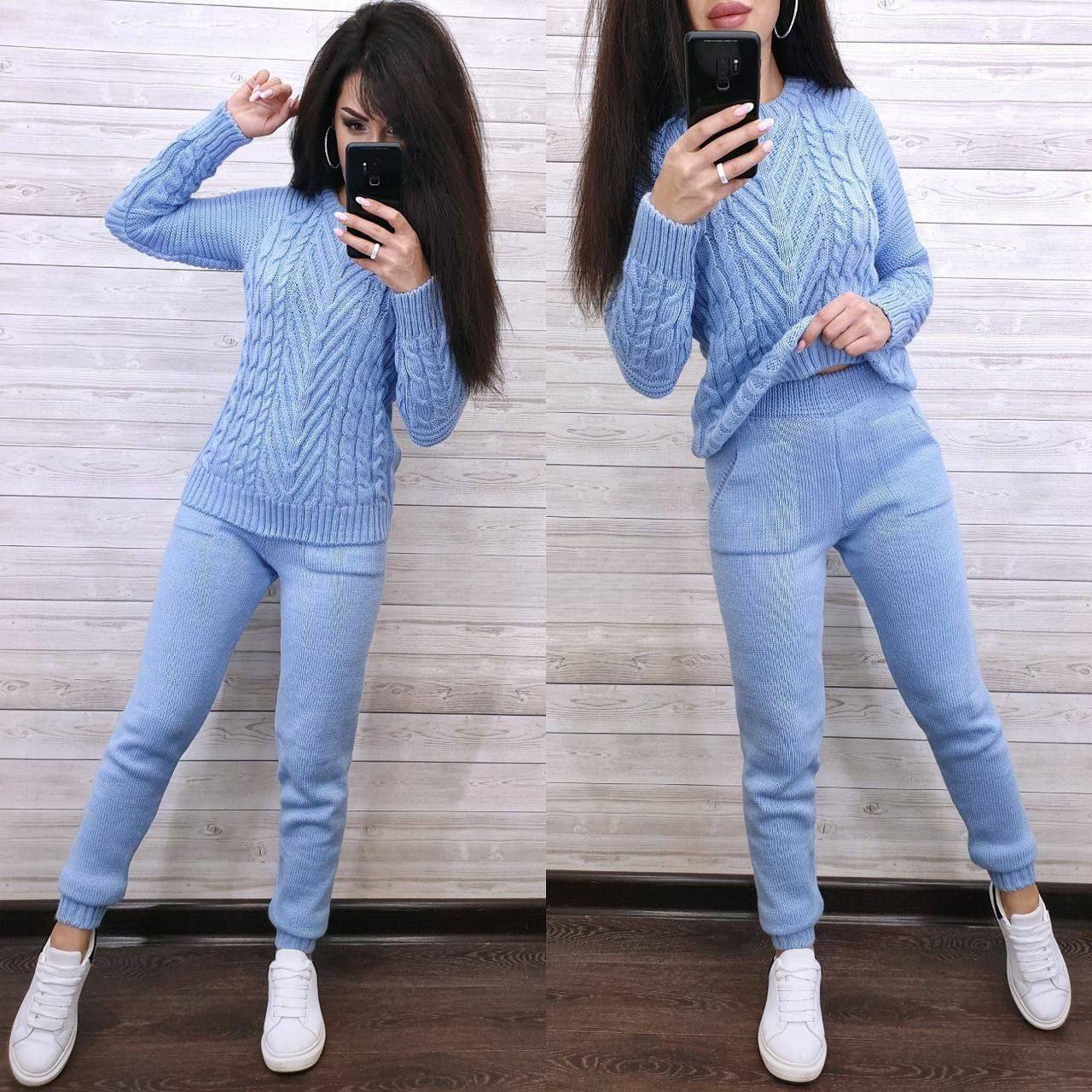 Woman wearing a light blue cable knit sweater and pants, standing in front of a mirror.