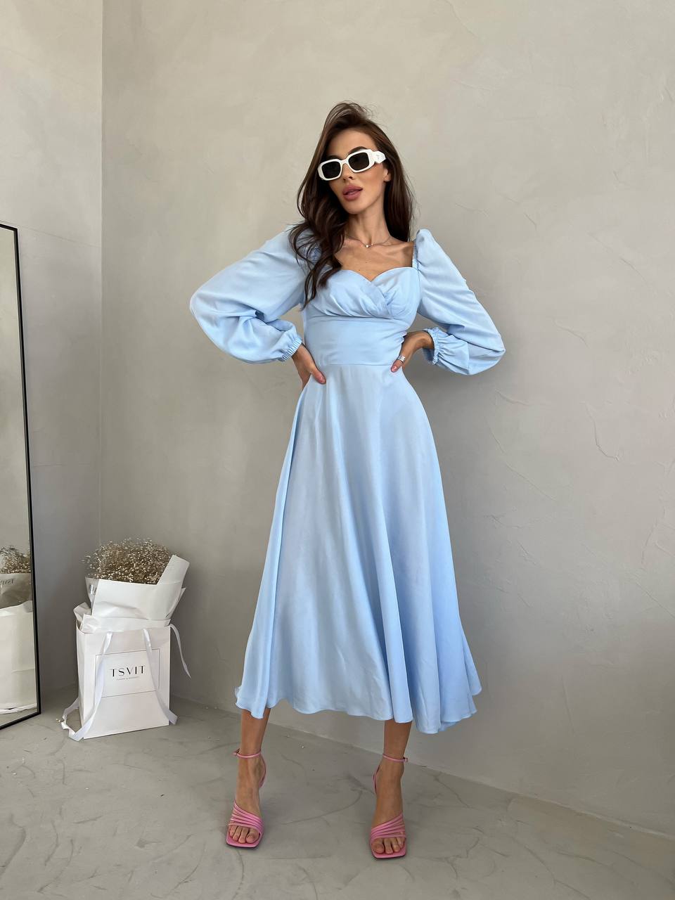 Woman wearing a light blue dress with long sleeves in a minimalistic setting.