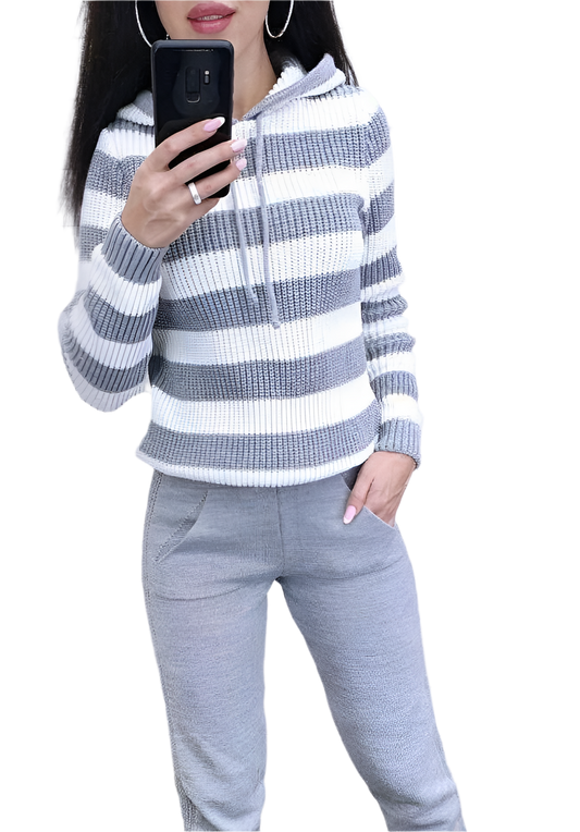 Person wearing a gray and white striped sweater and gray pants, holding a phone.