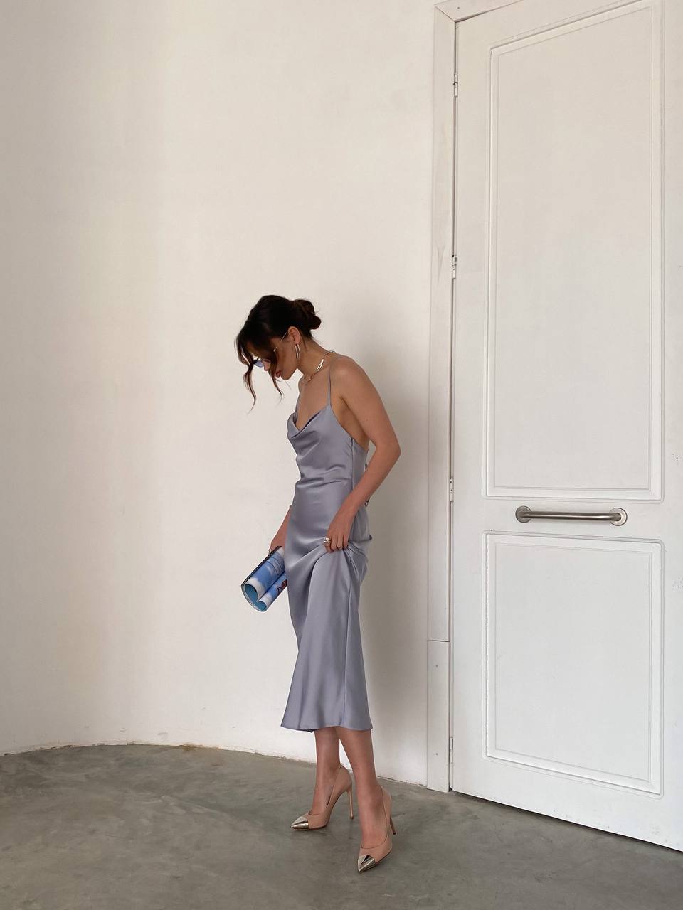 Woman in a silver dress standing in a minimalistic room with a white door.