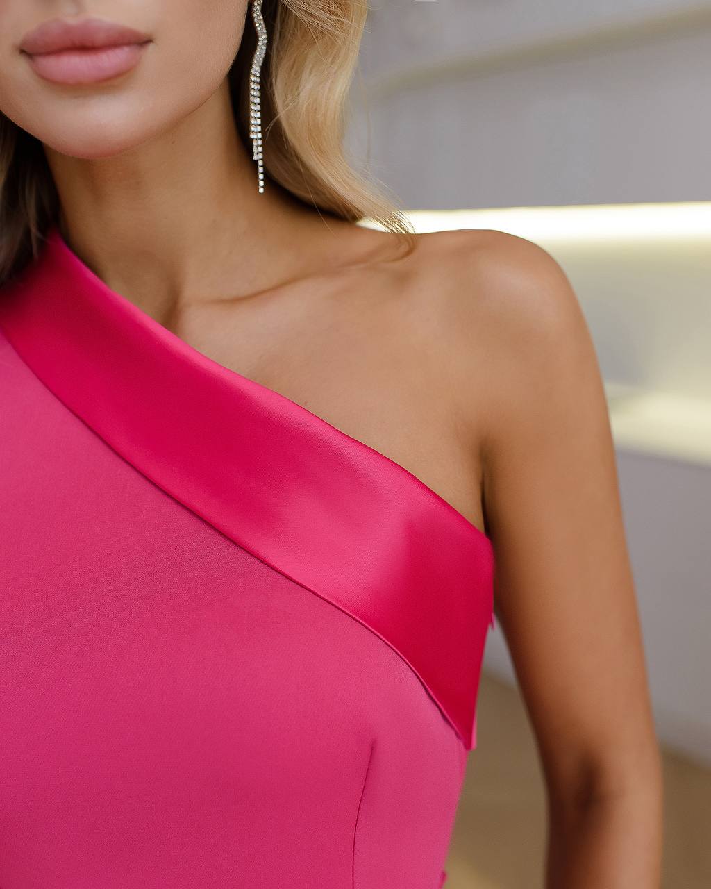Close-up of a person wearing a pink one-shoulder dress with a blurred background