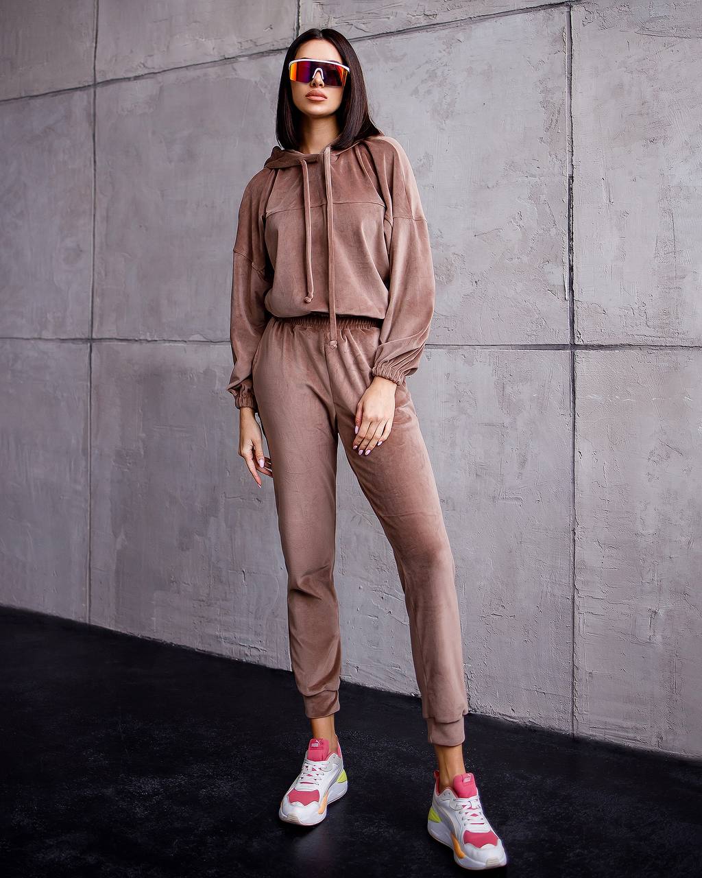Person wearing a brown tracksuit and colorful sneakers against a gray wall.