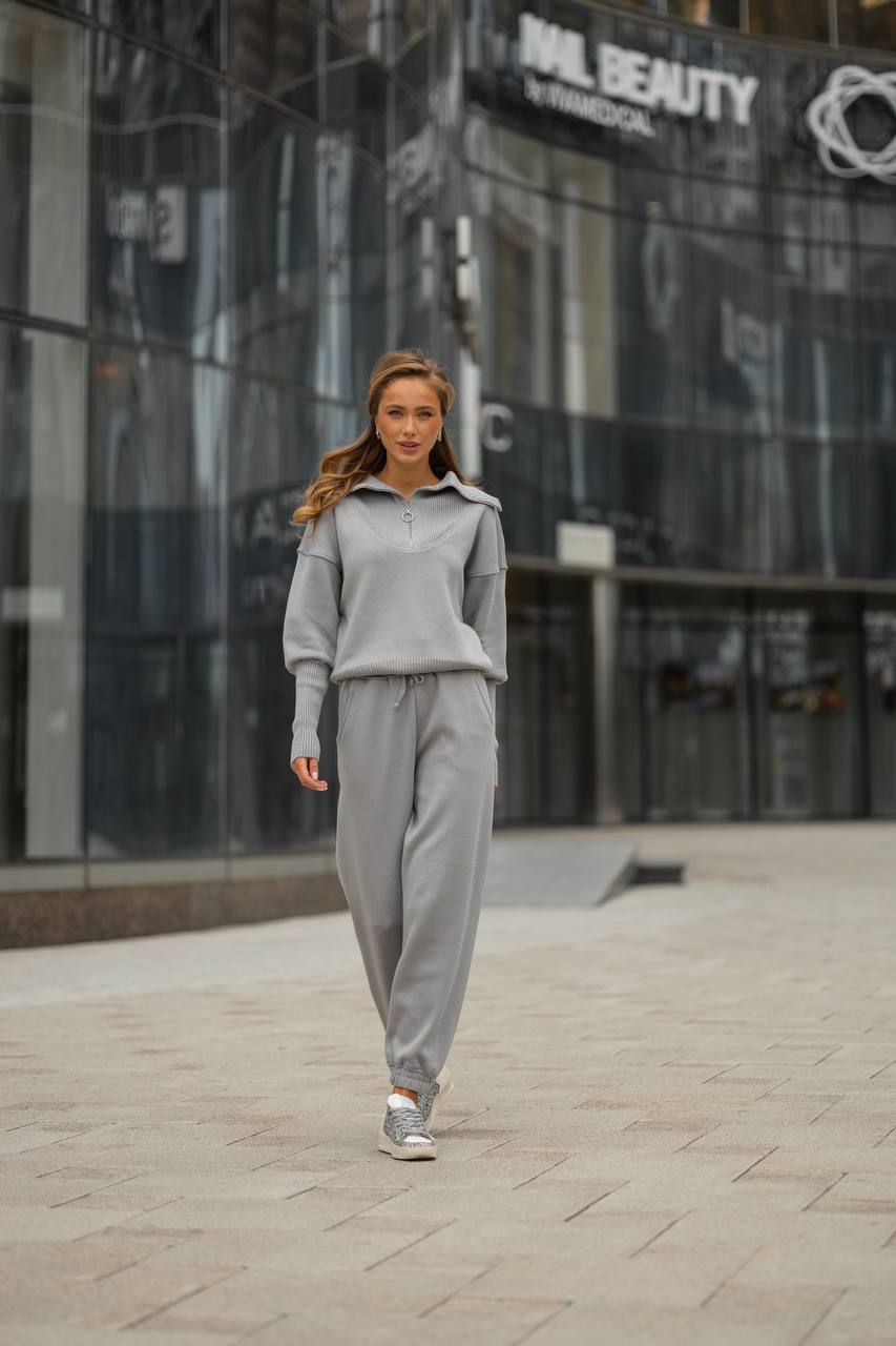 Woman in a gray tracksuit walking on a city street with modern buildings in the background.