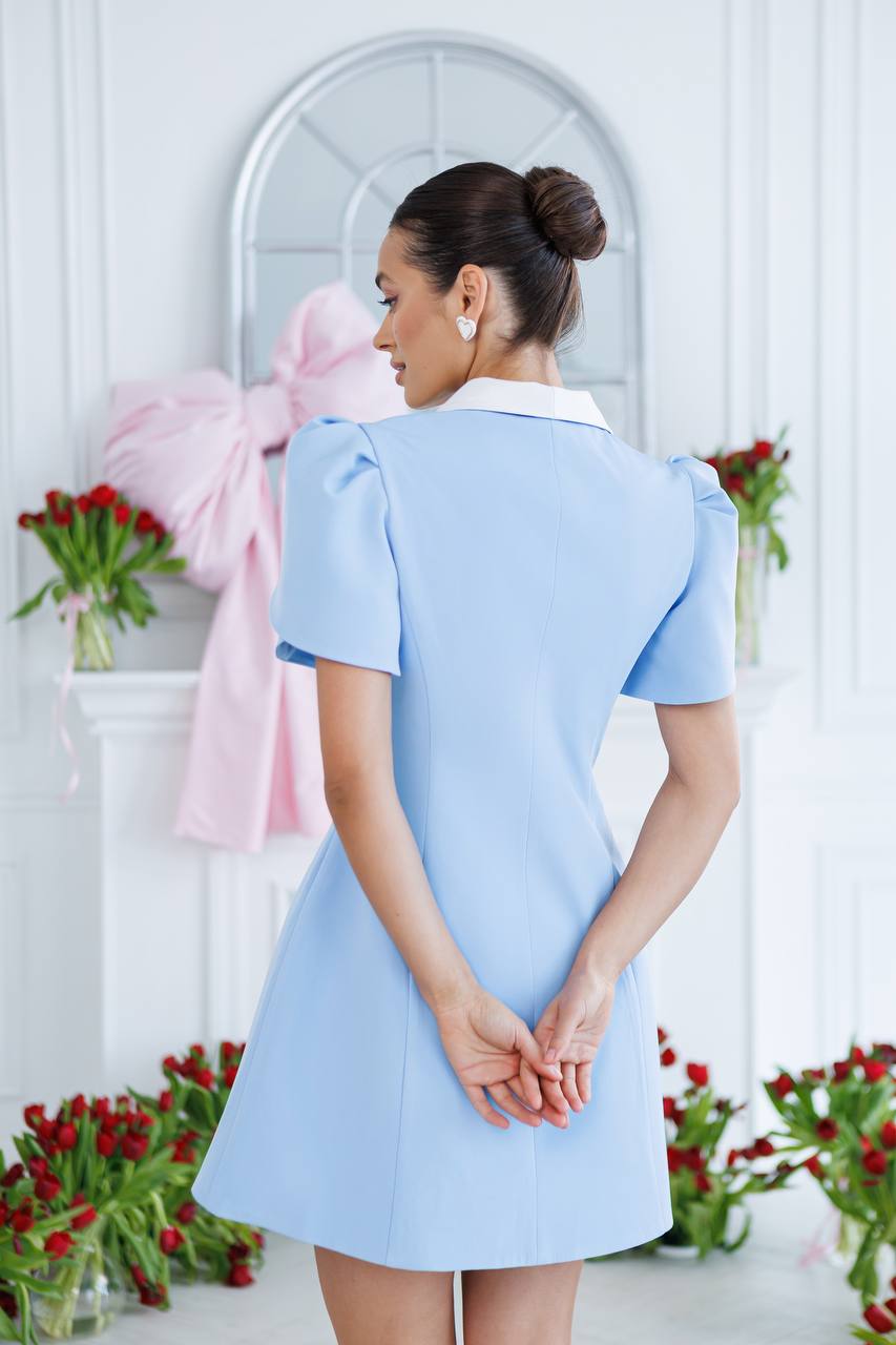 Woman wearing a light blue dress with a white collar in a decorated room.