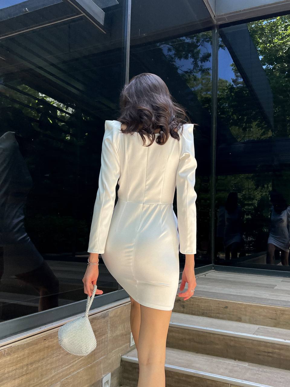 Woman in a white outfit standing on steps with a reflective glass wall in the background