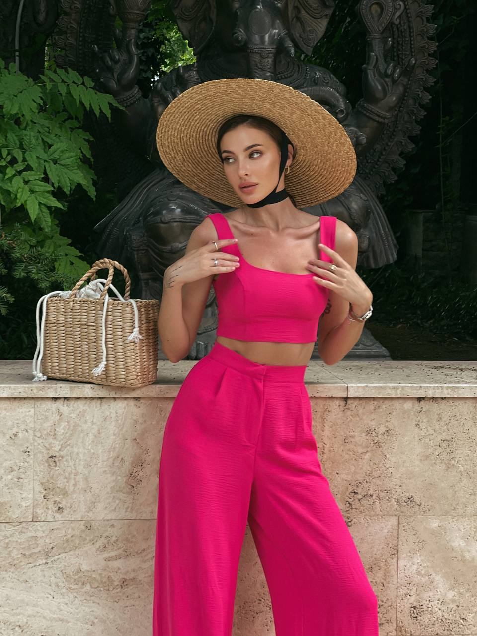 Woman in a bright pink outfit with a straw hat standing outdoors.