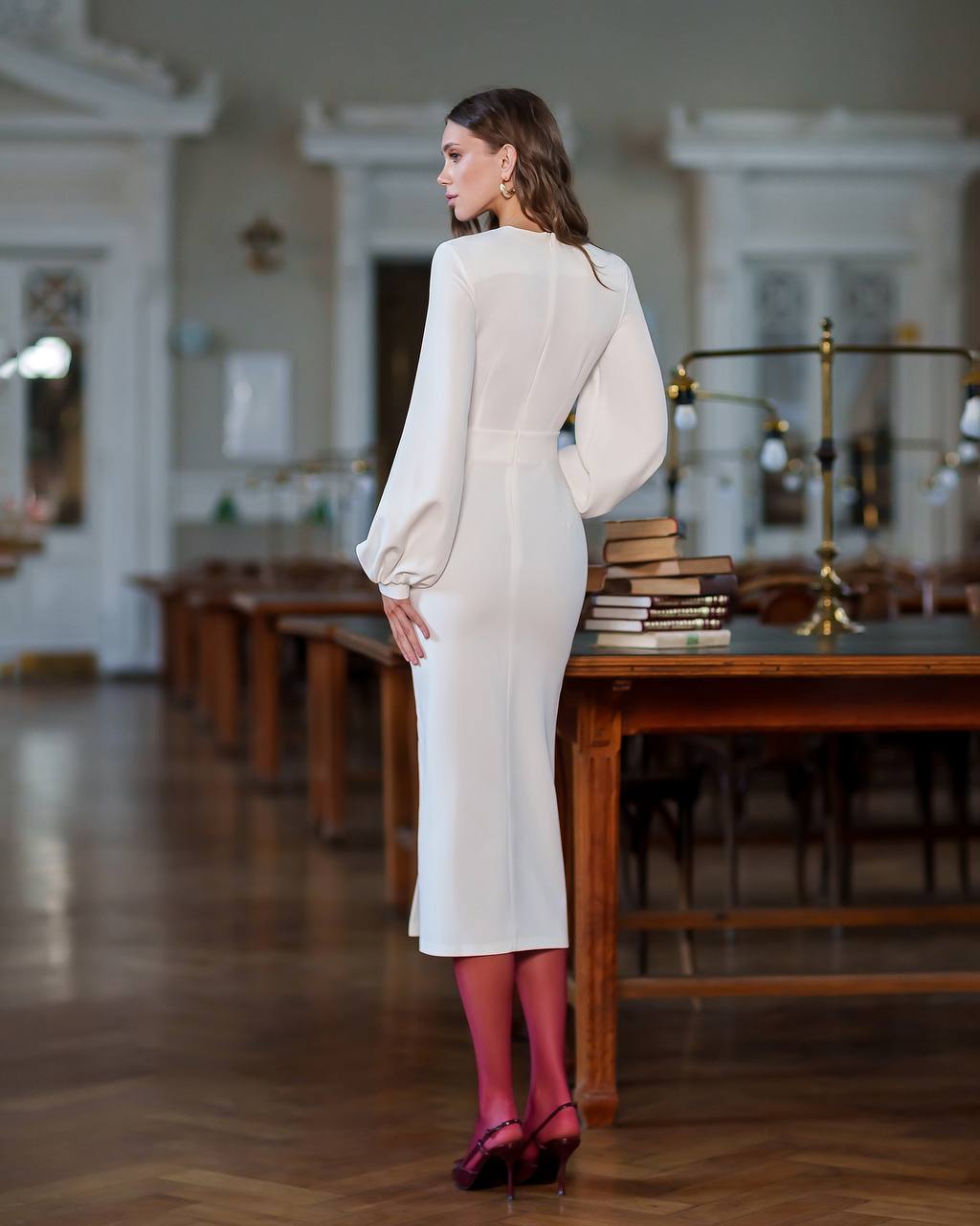 Woman in a white outfit standing in a room with wooden floors and furniture.