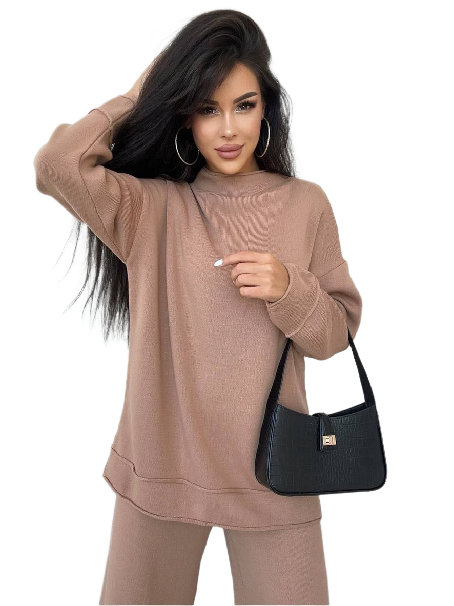Woman wearing a beige sweatshirt and pants holding a black handbag on a white background