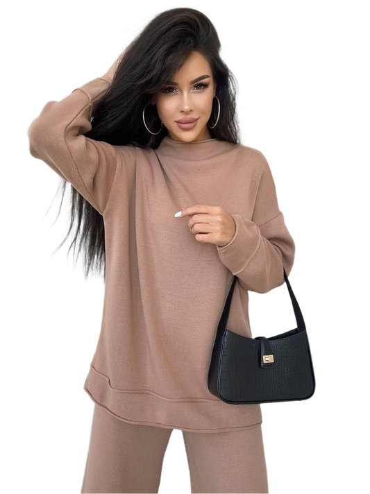 Woman wearing a beige sweatshirt and pants holding a black handbag on a white background