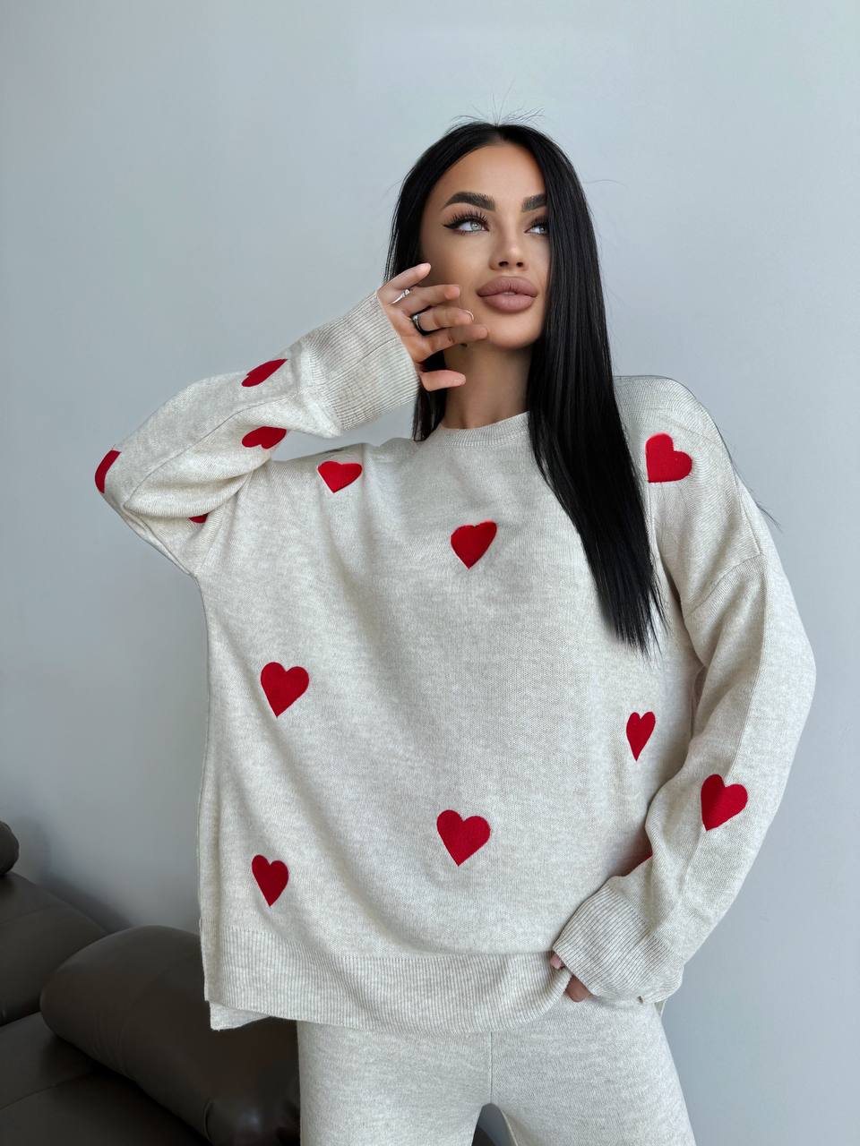 Woman wearing a white sweater with red heart patterns against a plain background