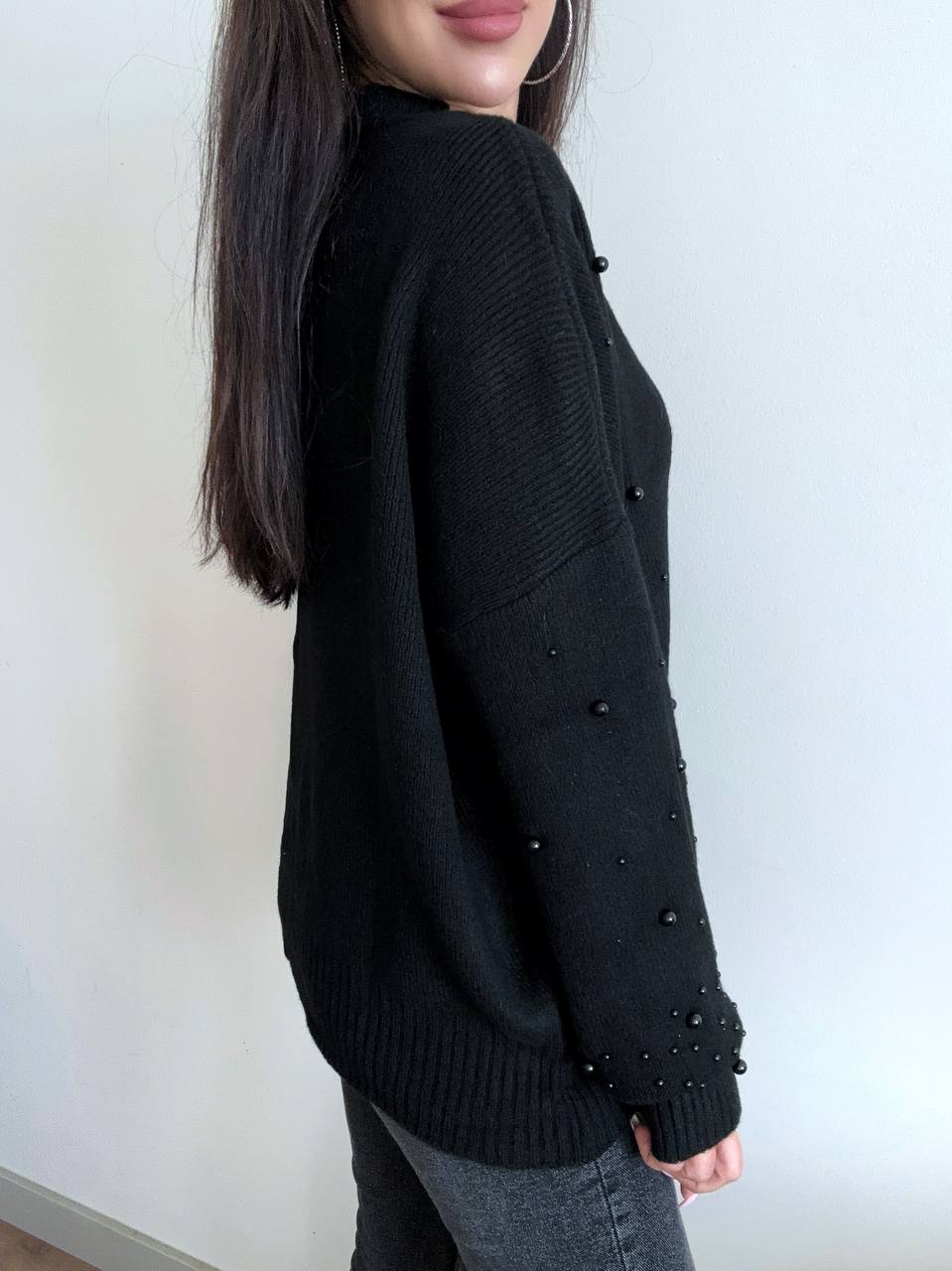 Person wearing a black sweater with button details against a white background