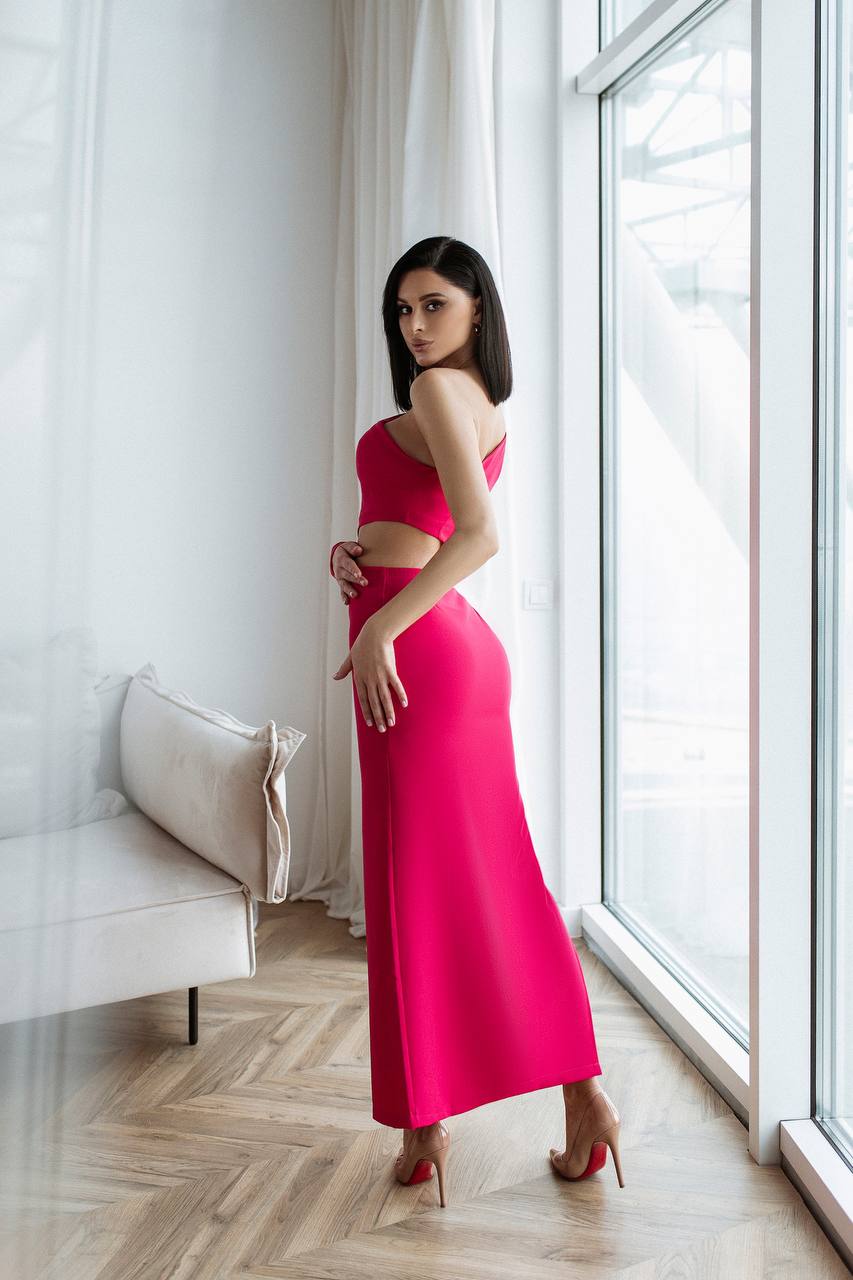 Woman in a pink dress standing in a room with large windows.
