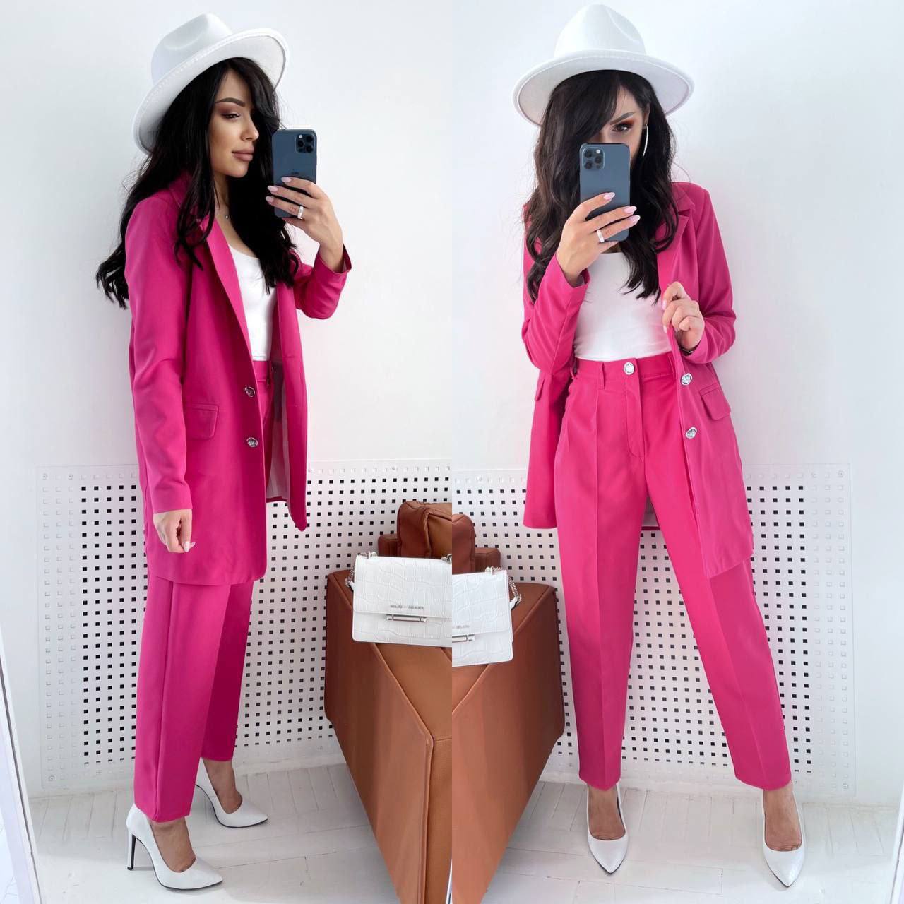 Woman in a pink suit taking a mirror selfie against a white wall.