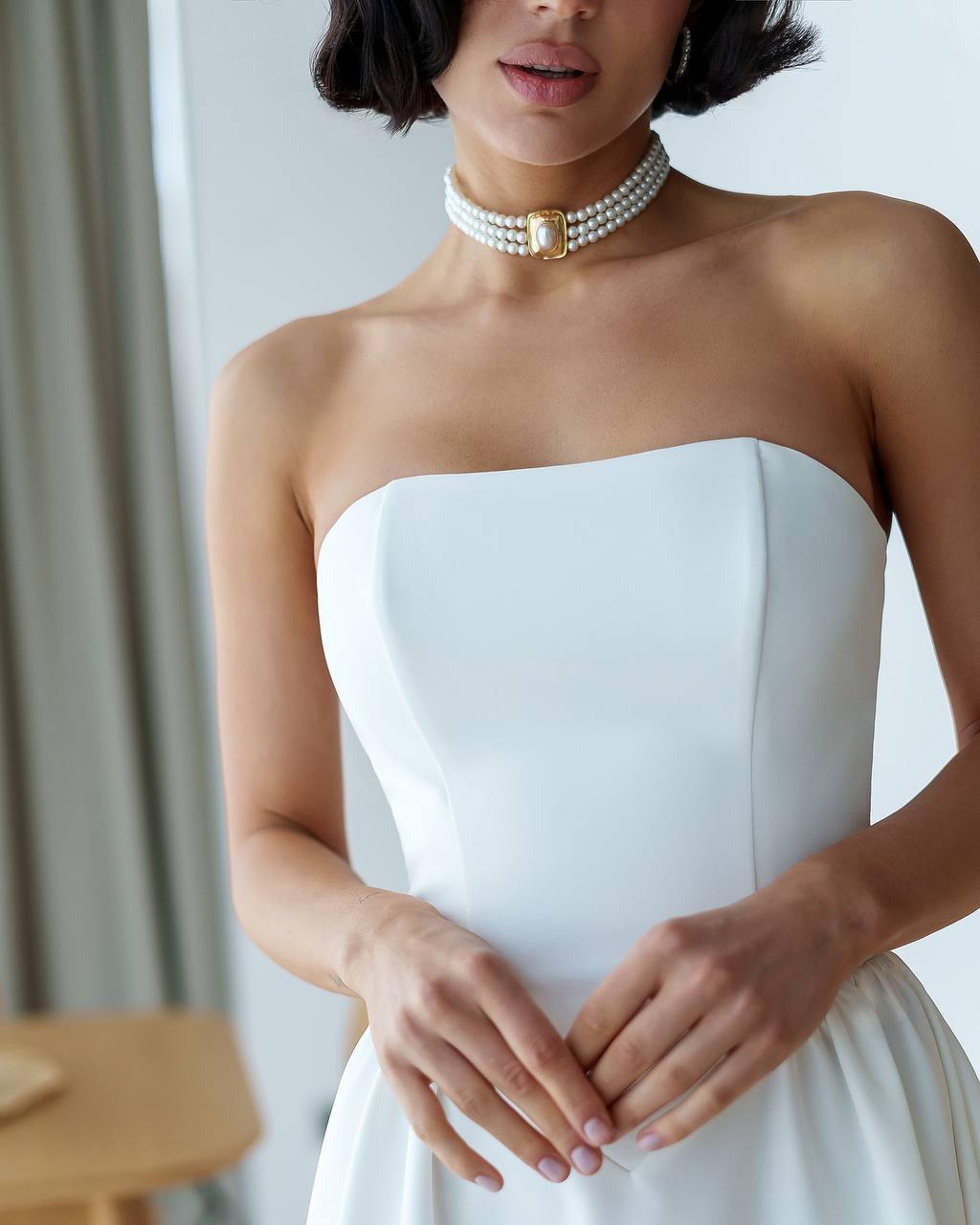Woman wearing a strapless white dress with a pearl necklace against a neutral background