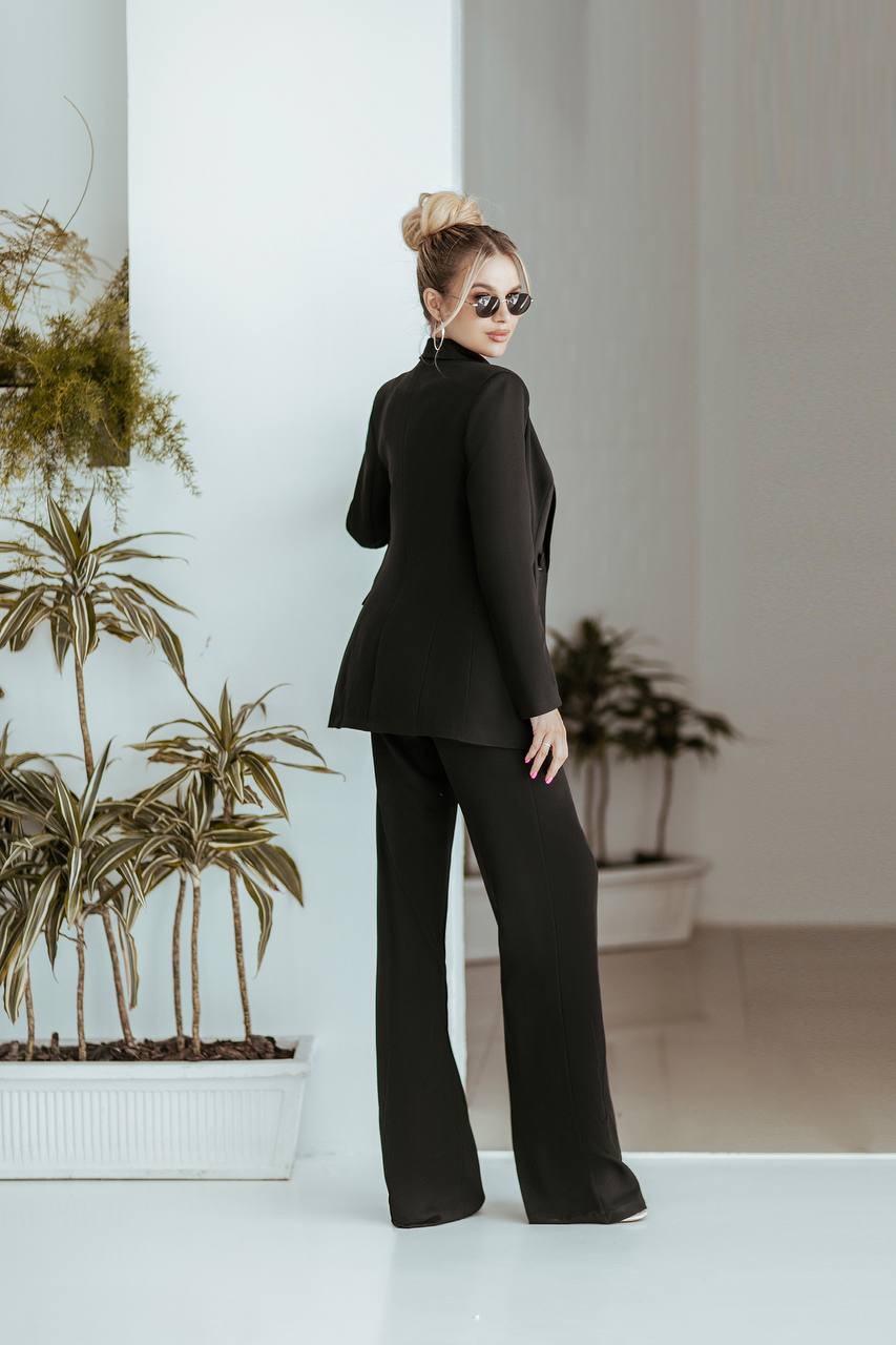 Woman in a black suit standing in a modern indoor setting with plants.