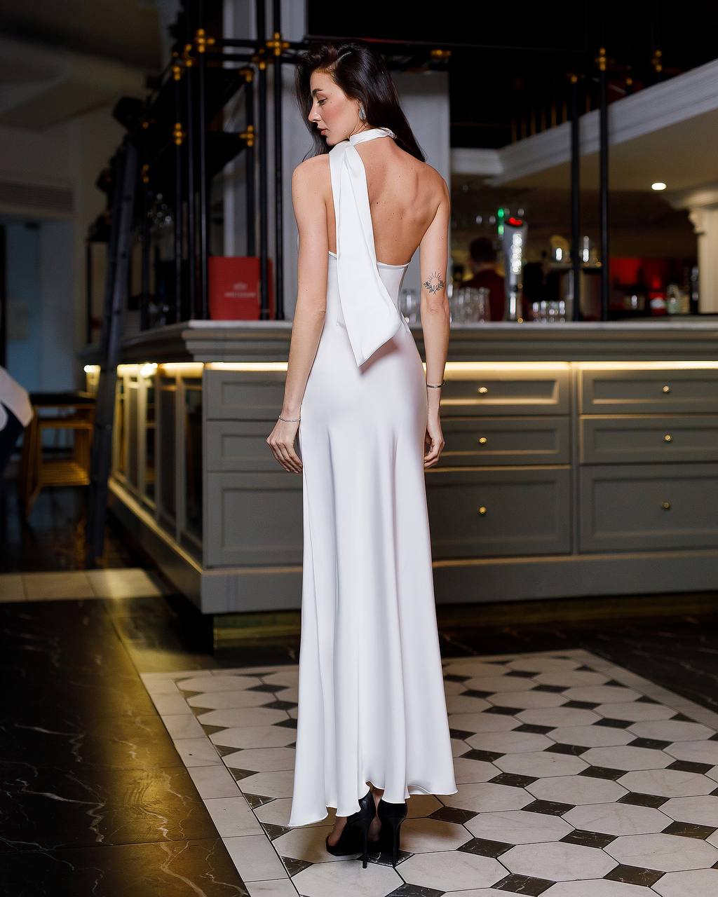 Woman in a white dress standing in a restaurant with a bar in the background