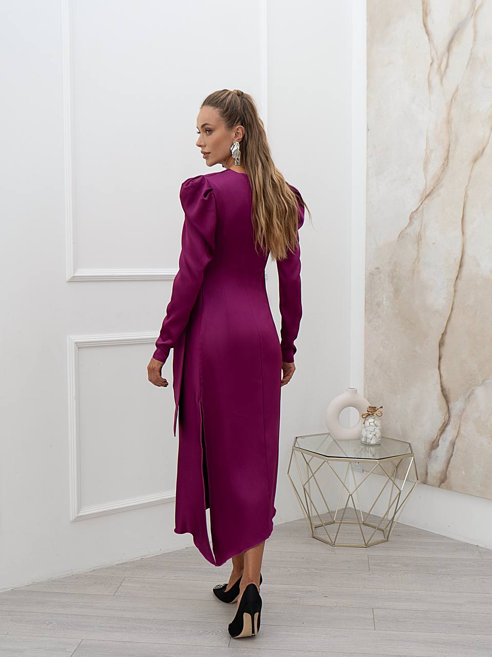 Woman in a purple dress standing in a room with a marble wall.