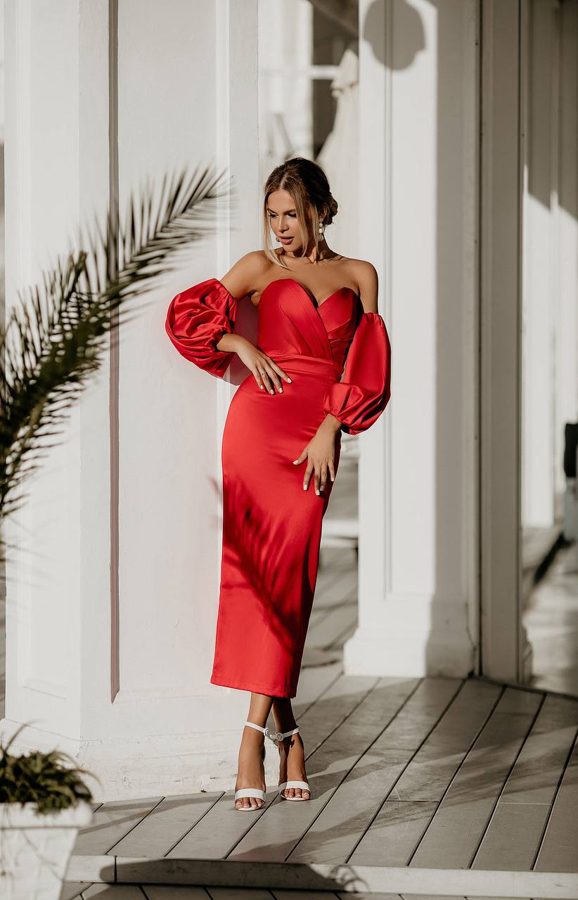 Woman in a red dress standing outdoors with a white building and palm leaves in the background