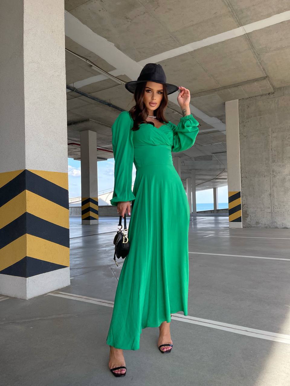 Woman in a green dress and black hat standing in an underground parking lot.
