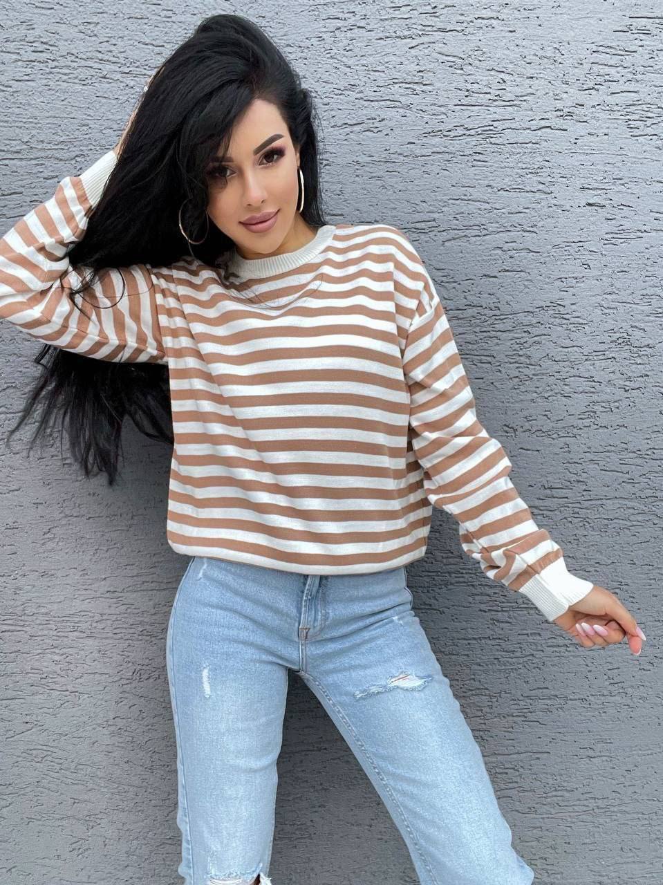 Woman wearing a striped sweater and jeans against a gray wall