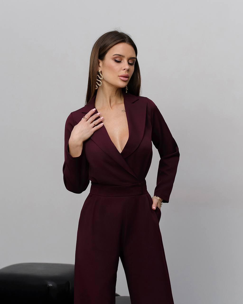 Woman wearing a burgundy jumpsuit against a gray background