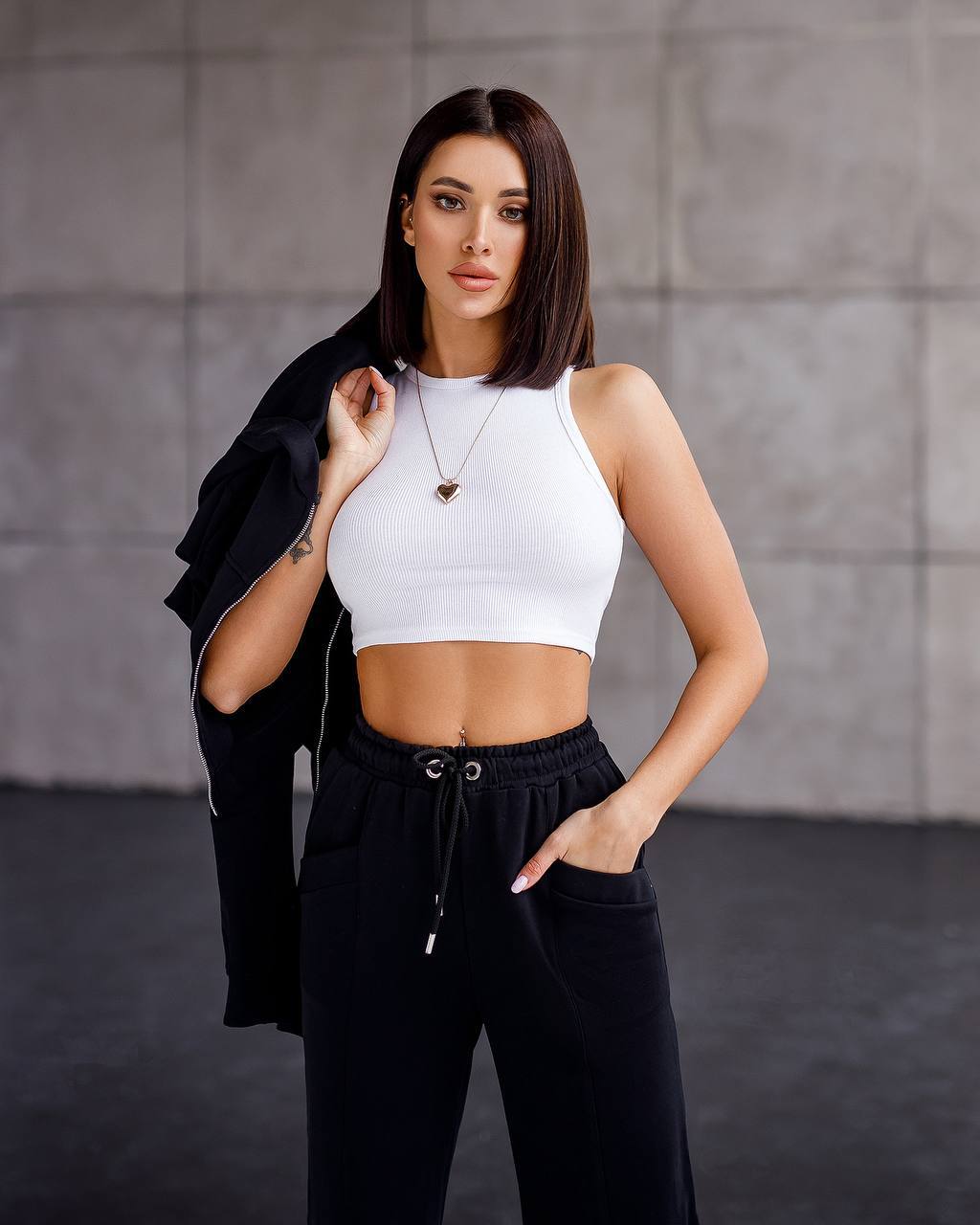 Woman wearing a white crop top and black pants against a gray background