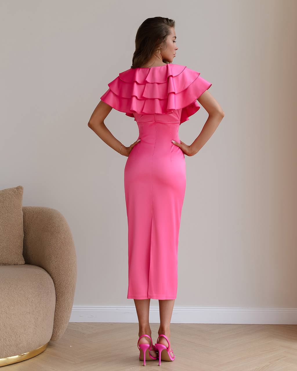 Woman wearing a pink dress with ruffled shoulders in a room with a beige sofa.