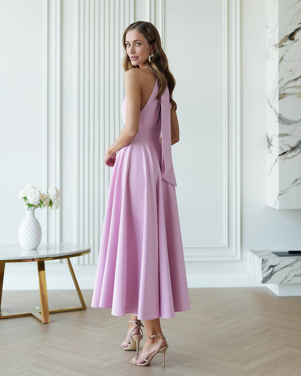Woman in a pink dress standing in a modern room with white walls and marble accents.