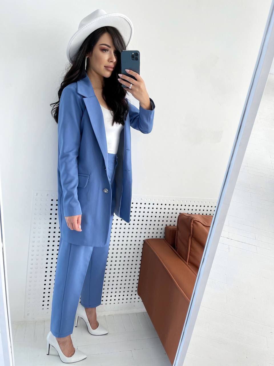 Woman in a blue suit taking a mirror selfie in a room with a brown couch.