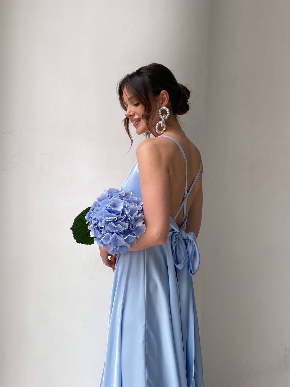 Woman in a light blue dress holding a bouquet of flowers against a plain background