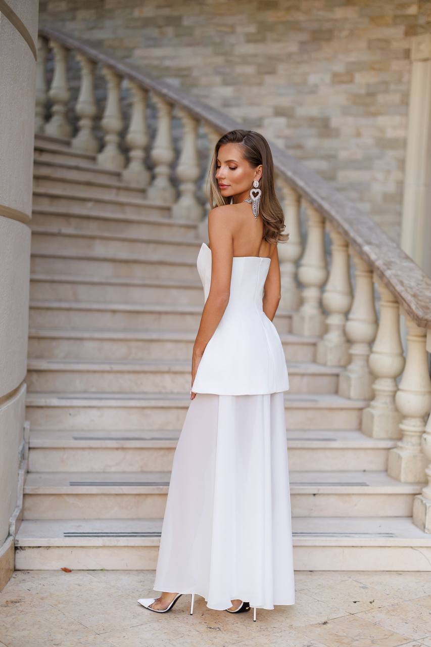 Woman in a white strapless dress standing on a staircase with stone walls.