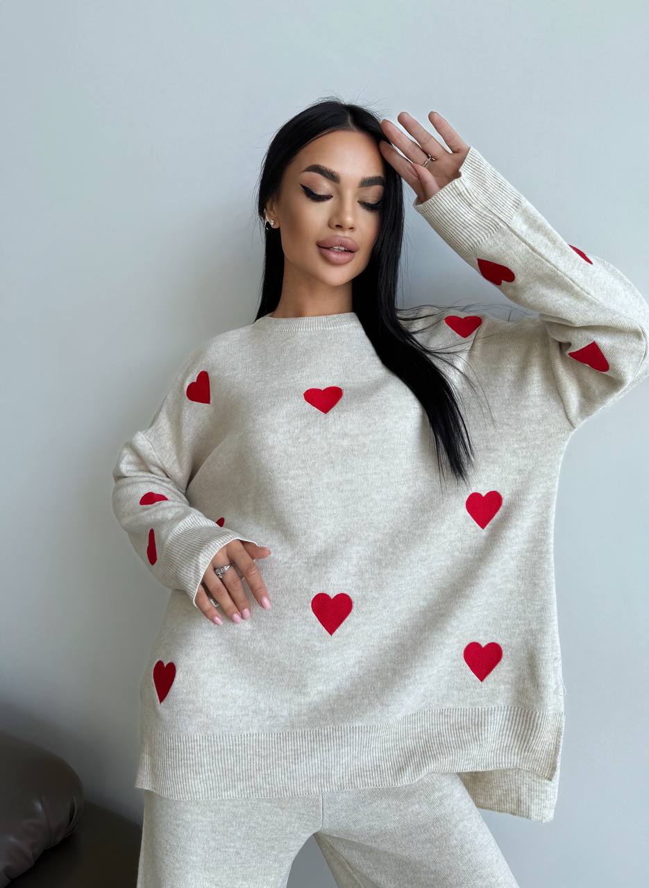 Woman wearing a cream sweater with red heart patterns against a plain background