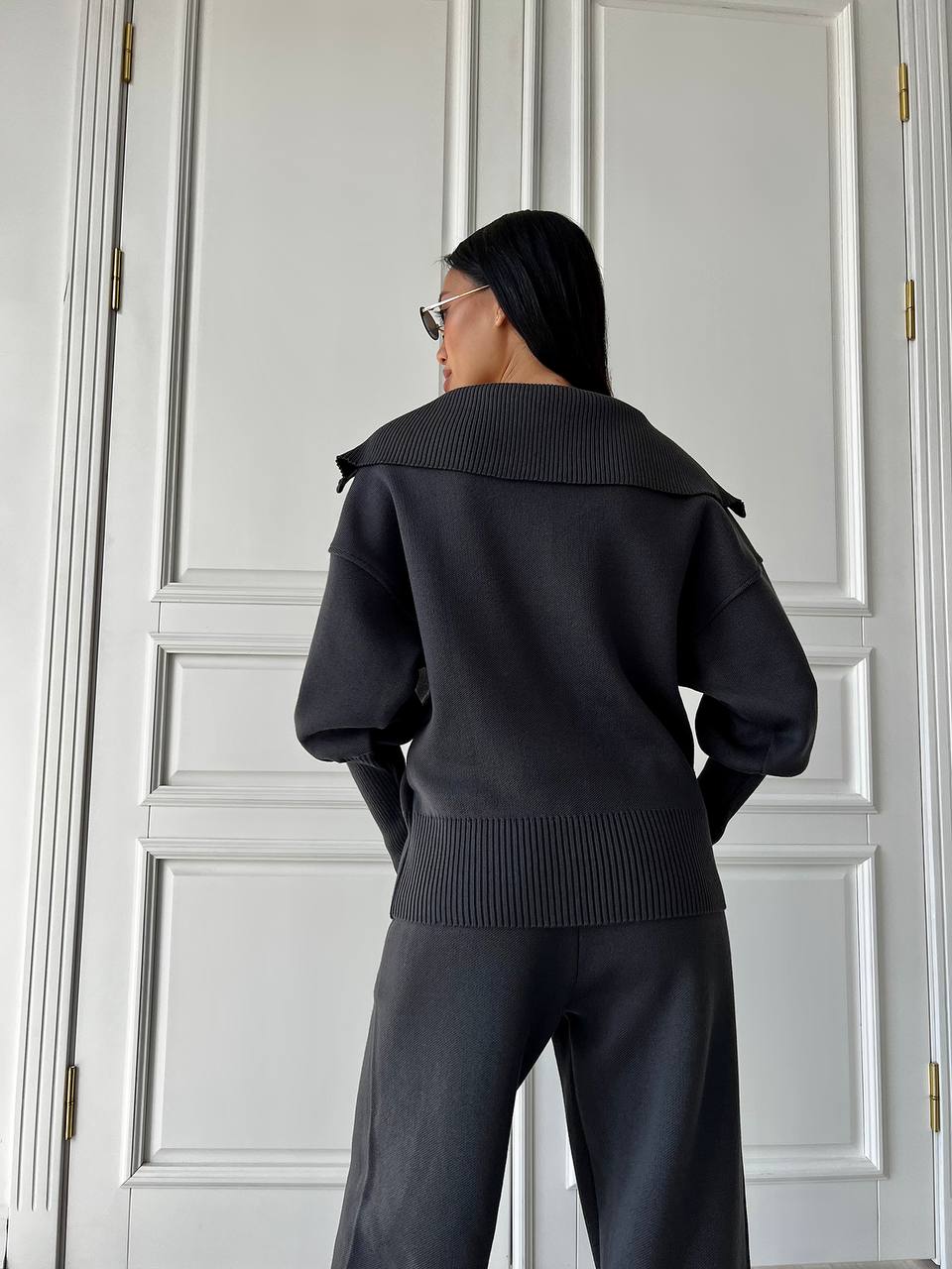 Person wearing a black outfit standing in front of a white paneled door.