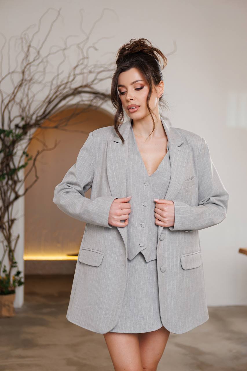 Woman wearing a gray suit standing indoors with a neutral background