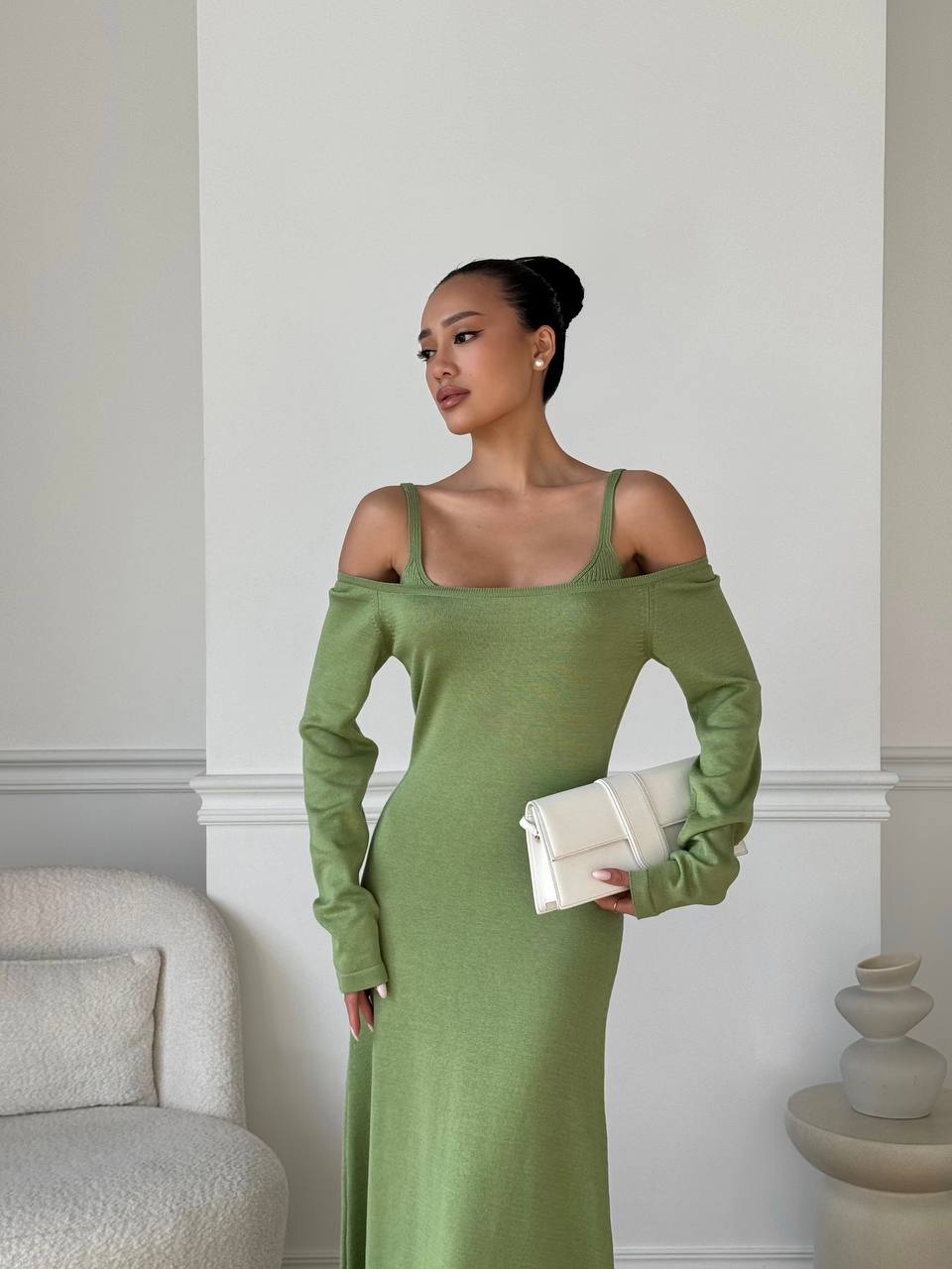 Woman in a green dress holding a clutch against a neutral background