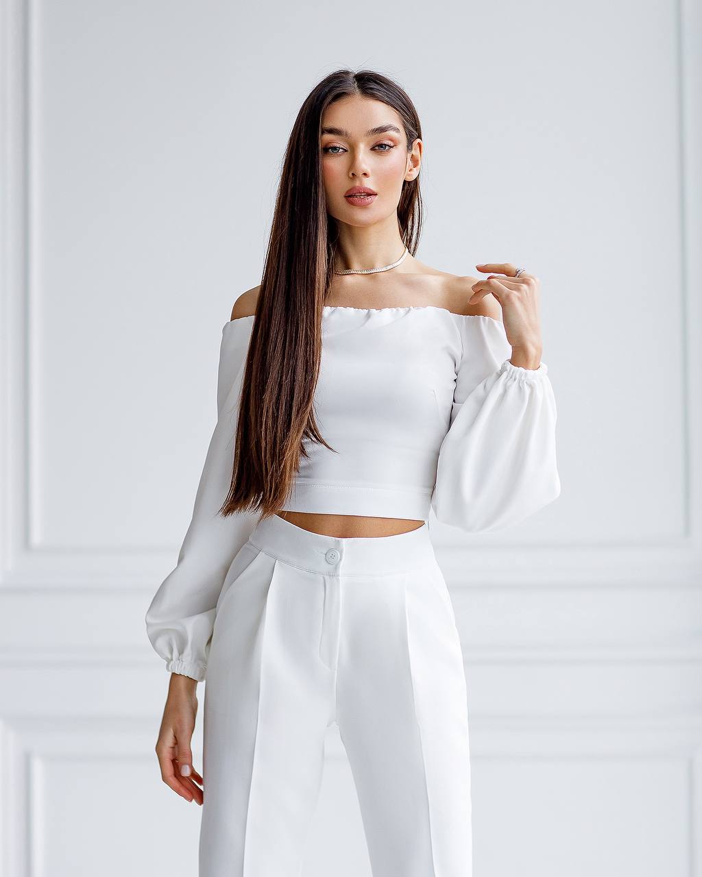 Woman wearing a white off-shoulder top and pants against a light gray background